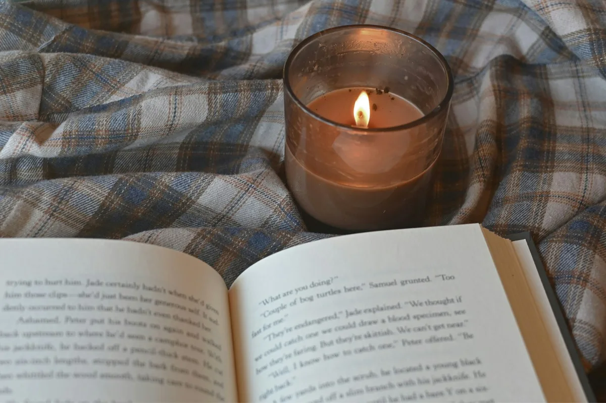 Vela acesa ao lado de um livro sobre uma manta, criando um ambiente acolhedor de oração