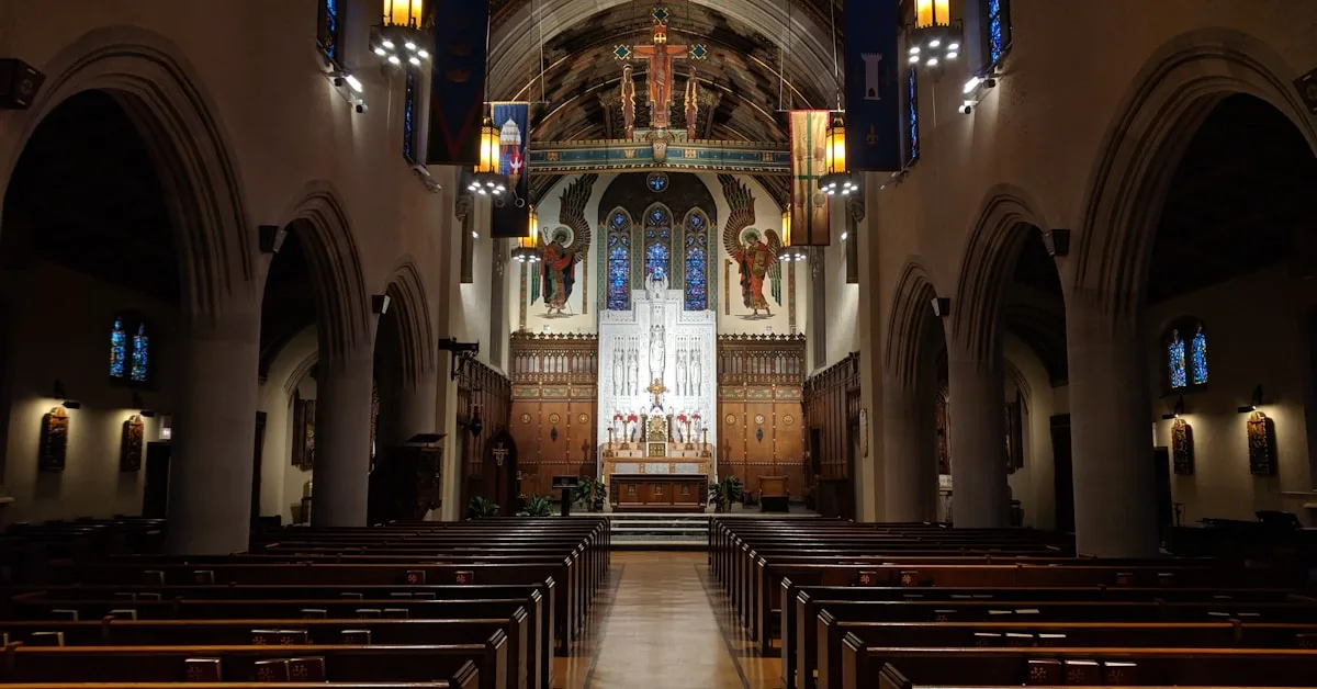 Interior de igreja católica com bancos de madeira e vitrais coloridos iluminados