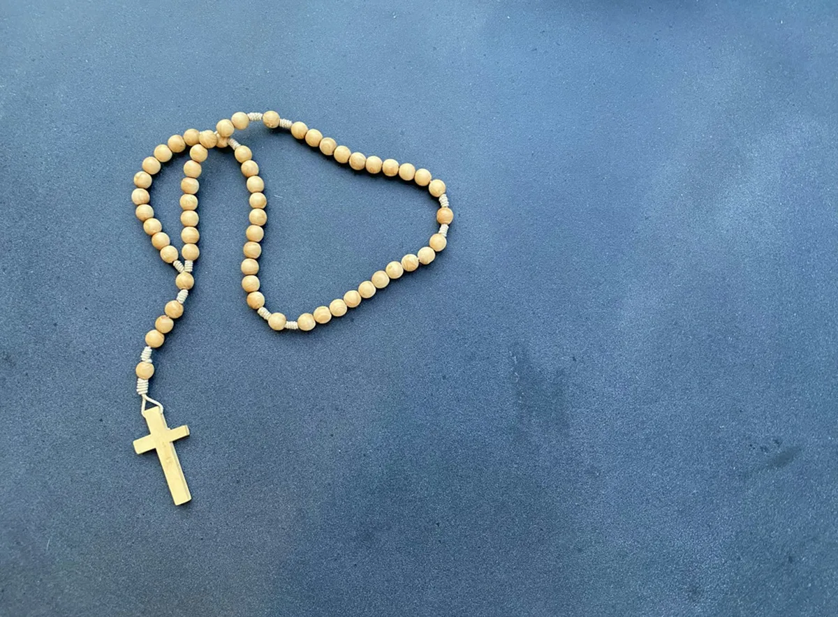 Terço católico de contas de madeira com crucifixo sobre superfície escura