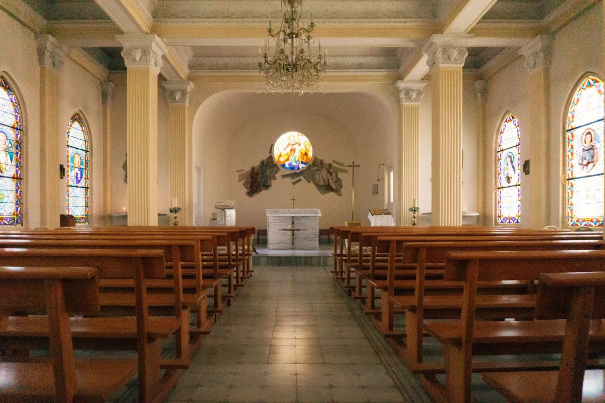 Interior tranquilo de igreja católica com bancos de madeira e altar ao fundo