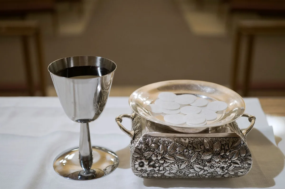 Bíblia aberta ao lado de vela acesa, com pão e vinho, símbolos da Eucaristia celebrada em Corpus Christi