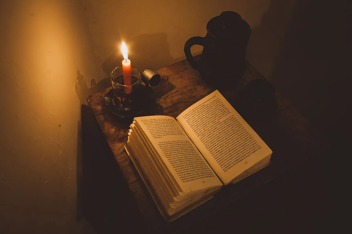 Vela acesa ao lado de um livro aberto sobre uma mesa, simbolizando oração e estudo