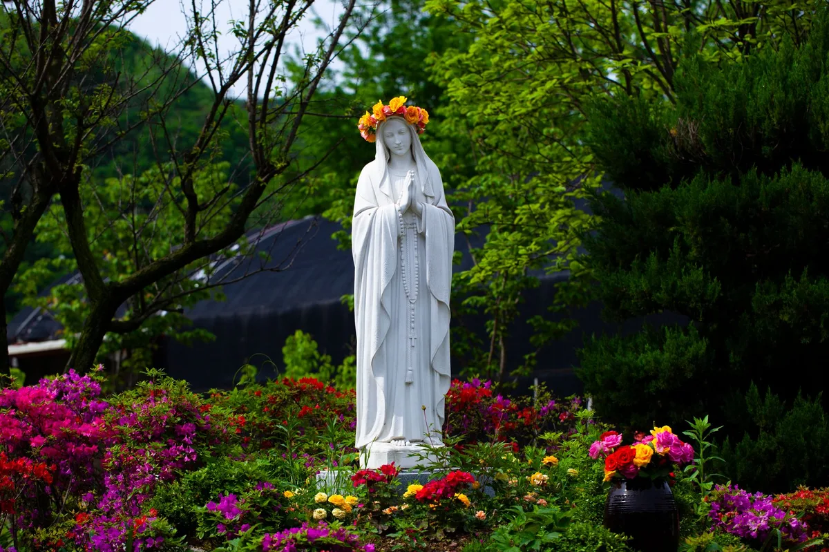 Imagem de Nossa Senhora em pedra, com coroa, contra o céu azul