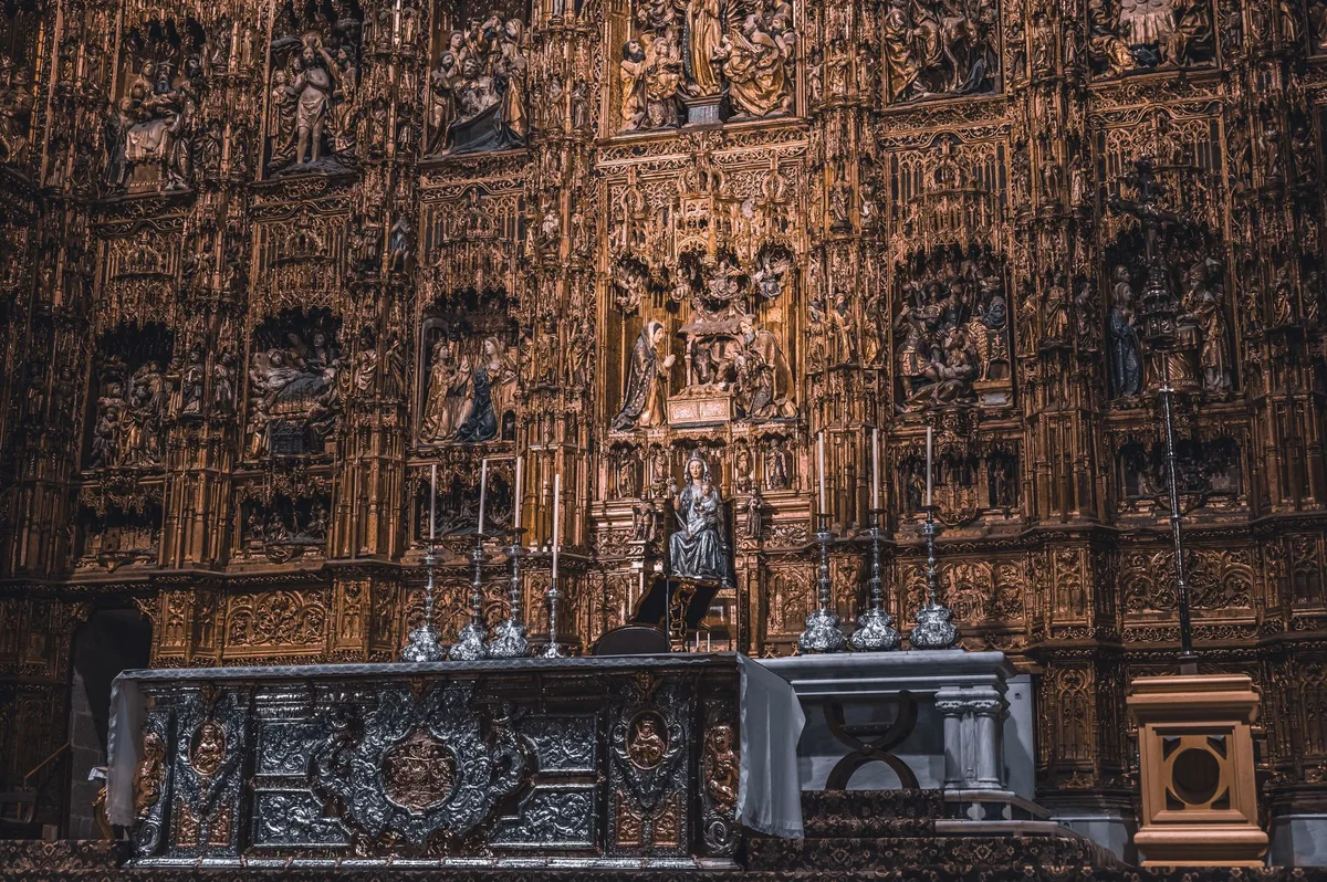 Interior solene de catedral católica com decoração dourada e arquitetura que evoca a história dos santos