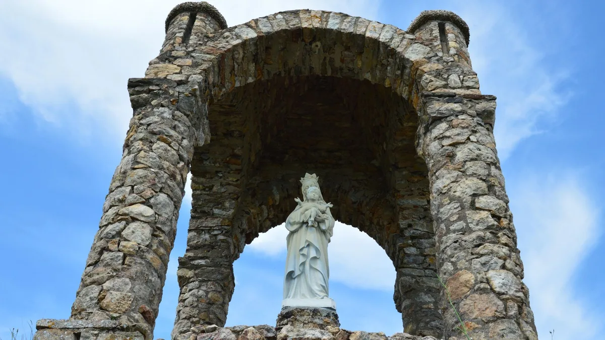 Estátua de santo sob o céu azul, evocando devoção e contemplação